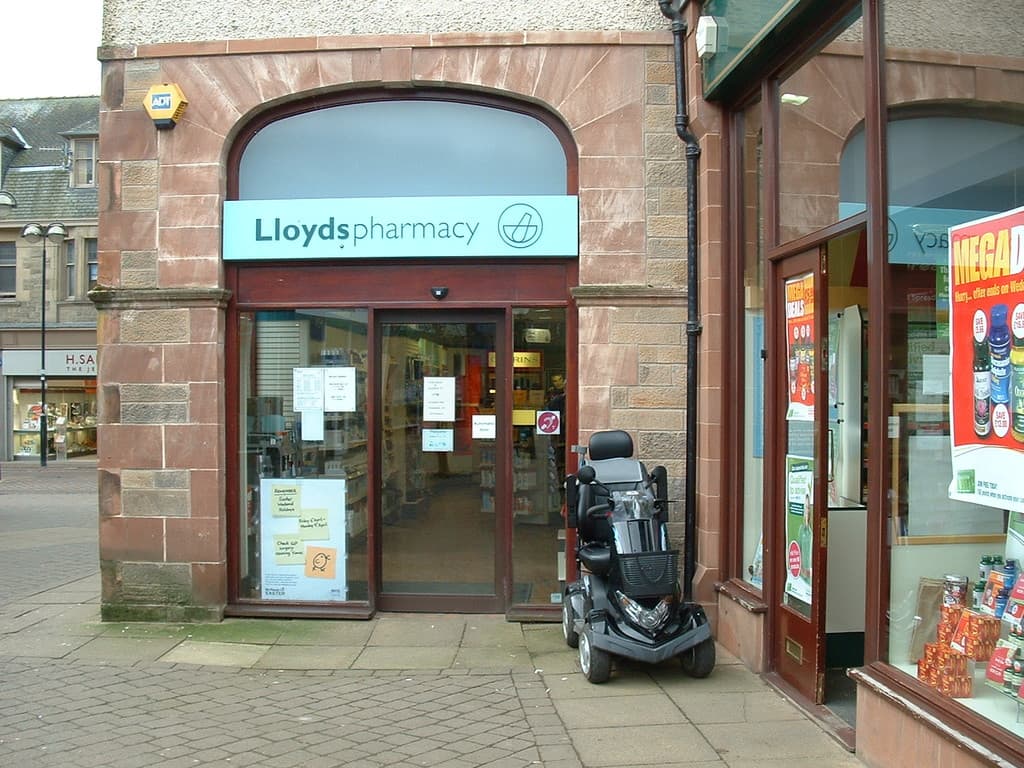 Ein Apothekenladen mit einem vor ihm geparkten Fahrzeug und einem Gebäude in der linken Ecke.