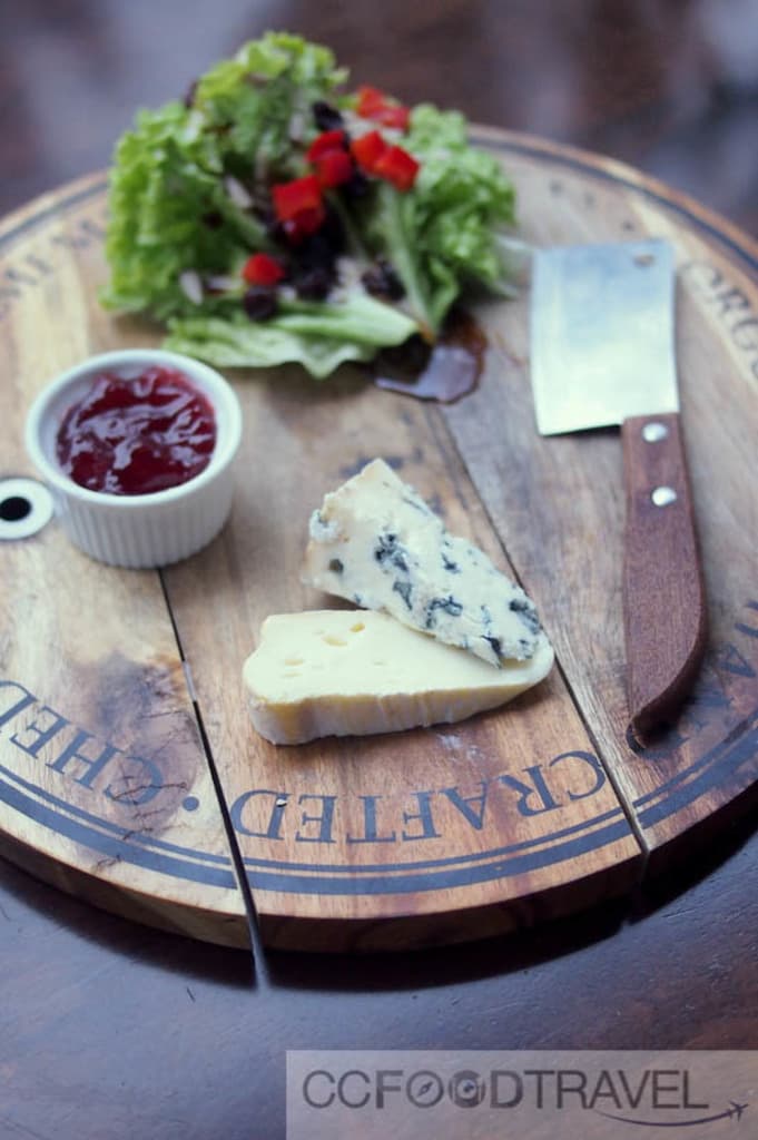 Ein hölzernes Schneidbrett mit Blattgemüse, einem Becher, einem Messer und etwas Essen, mit Text unten.