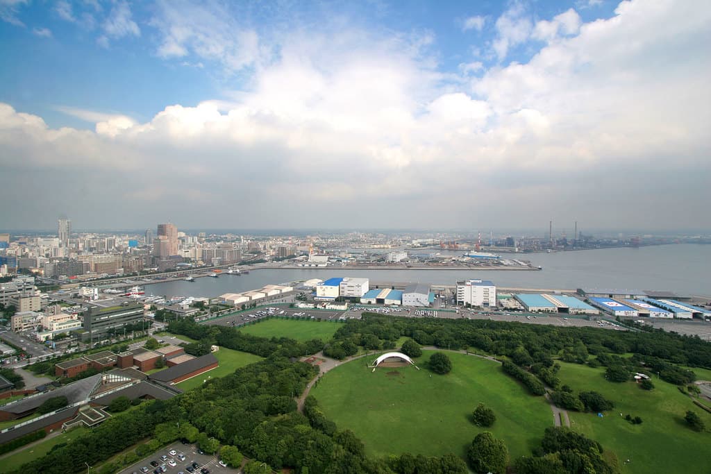 Eine Luftansicht einer Stadt mit einem großen Garten, umgeben von Gebäuden, Häusern, Straßen und einem Meer auf der rechten Seite.
