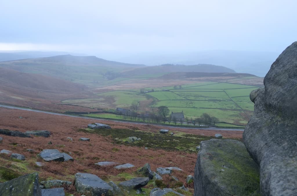 Eine malerische Landschaft mit großen Felsen und Steinen im Vordergrund und Feldern und Bergen im Hintergrund.