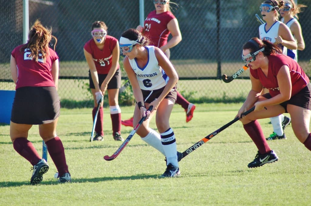 Frauen spielen Hockey auf einem Rasenfeld mit einem Netz als Hintergrund.