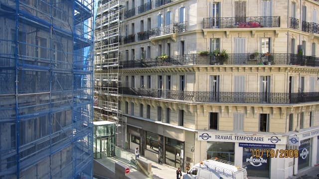 Ein Bus steht auf einer Straße mit einer Wand, Strommasten mit Kabeln, Bäumen, Gebäuden und dem Himmel im Hintergrund.
