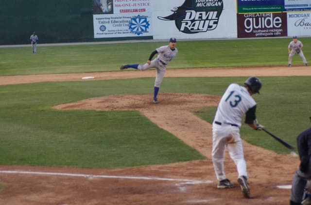 Eine Gruppe von Menschen spielt Baseball auf einem Feld mit Bannern im Hintergrund.