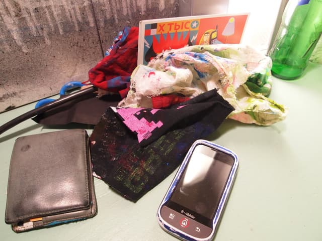 Tuchstücke, ein Handy und eine Geldbörse sind auf einer Oberfläche angeordnet.