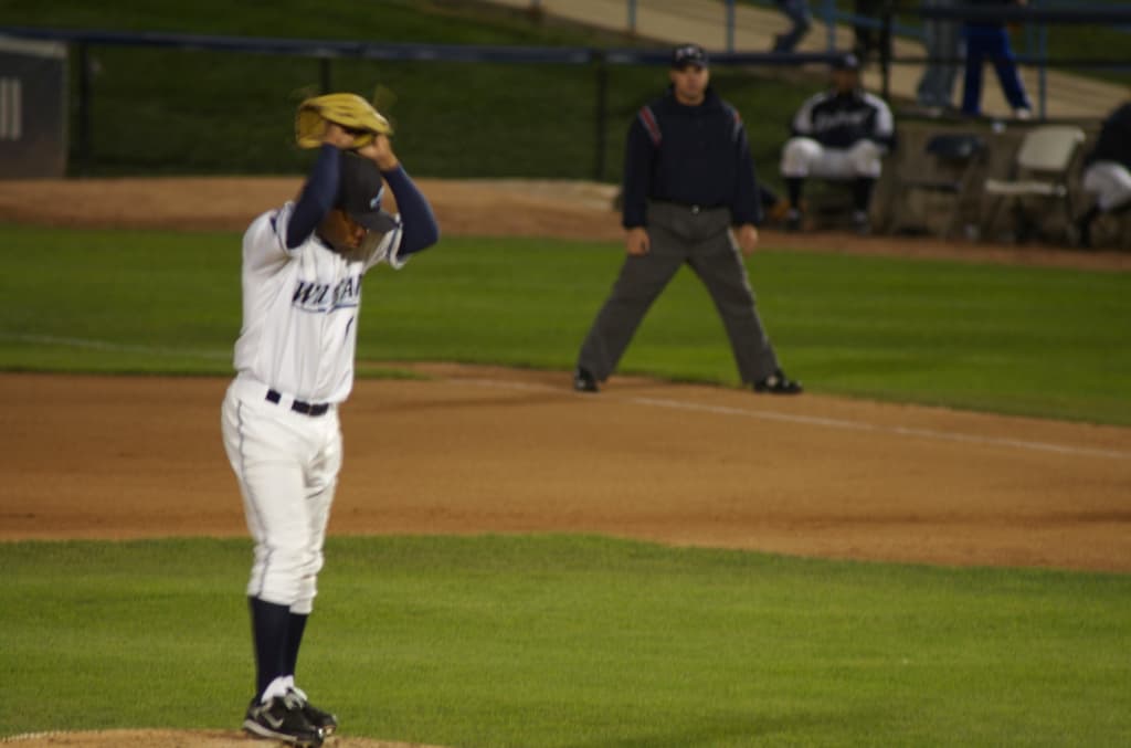 Eine Gruppe von Menschen, die ein Spiel im Freien spielen, mit anderen im Hintergrund auf Stühlen sitzend, umgeben von einem Zaun und Gras.