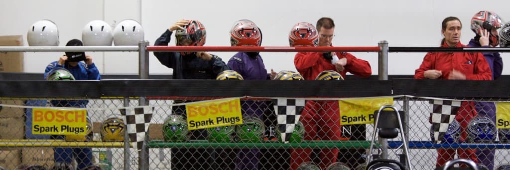 Ein Maschendrahtzaun mit Plakaten und Fahnen, mit ein paar Menschen im Hintergrund, einige tragen Helme, und zusätzliche Helme auf einem Ständer, alles vor einer Wand.