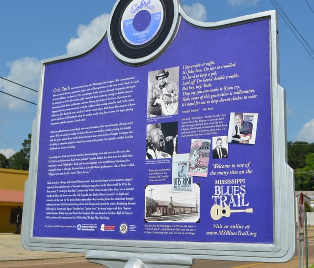 Ein Informationsbrett, Gebäude, ein Schuppen, Bäume, Stromkabel und ein bewölkter Himmel.