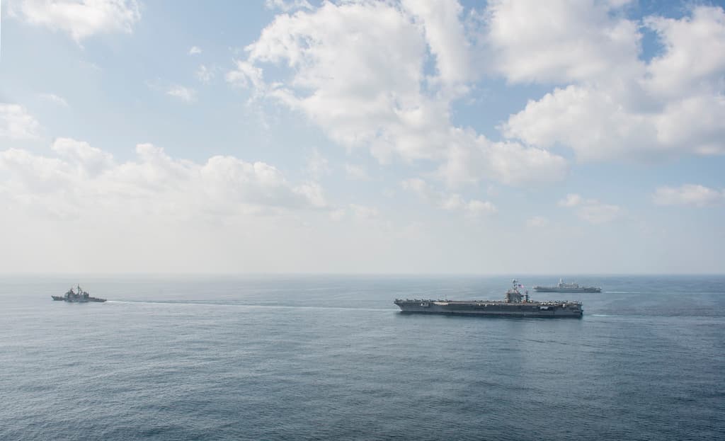 Drei Schiffe segeln auf einem Gewässer unter einem bewölkten Himmel.