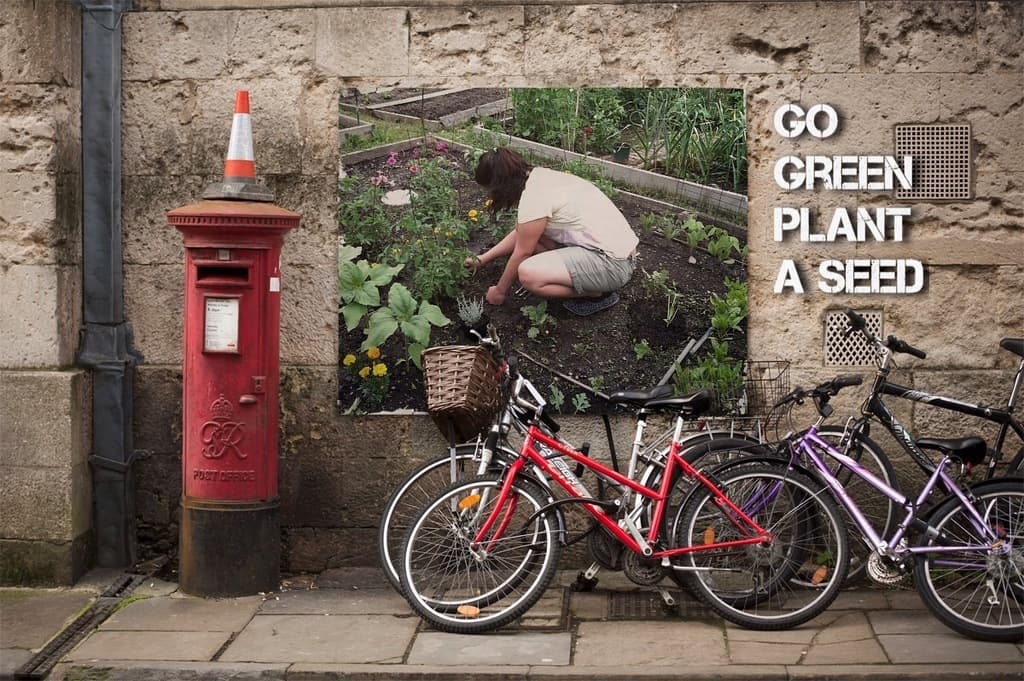 Mehrere Fahrräder sind in der Nähe einer Briefkasten mit einer Sicherheitskegel auf der Spitze geparkt, mit einem Plakat an einer Wand im Hintergrund und einem Weg am unteren Rand des Bildes.