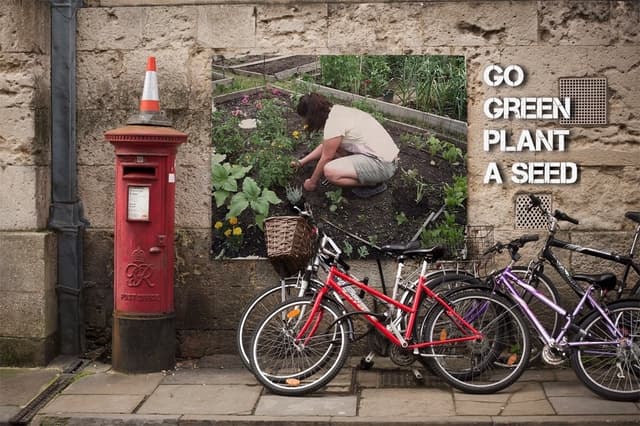 Mehrere Fahrräder sind in der Nähe einer Briefkasten mit einer Sicherheitskegel auf der Spitze geparkt, mit einem Plakat an einer Wand im Hintergrund und einem Weg am unteren Rand des Bildes.