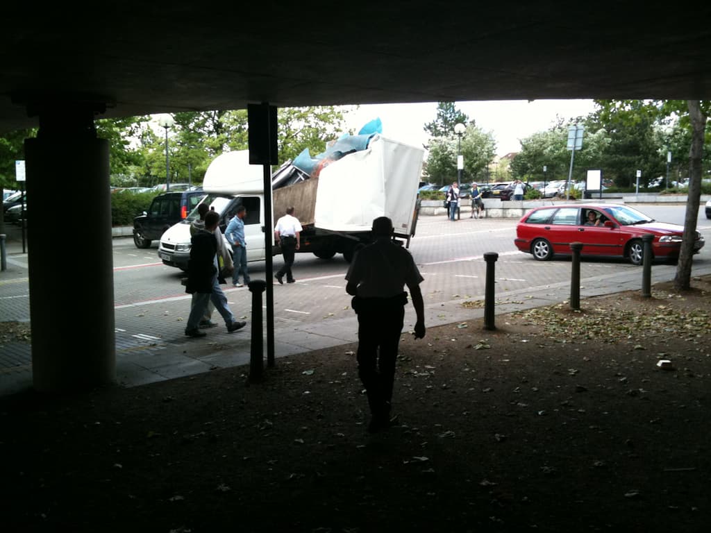 Eine belebte Straßenszene mit zahlreichen Fußgängern, einem Auto und einem Lastwagen auf der Straße.