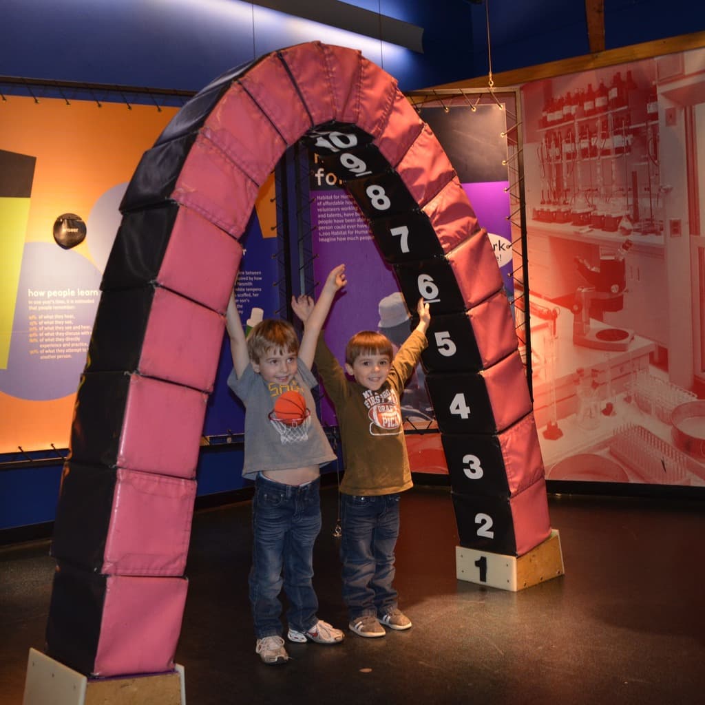 Kinder spielen auf einem lustigen Fahrgeschäft mit Brettern, vor einem Boden.