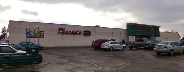 Ein bewölkter Himmel mit einer Wand und Brettern auf der linken Seite und Fahrzeugen einschließlich eines Wagens auf der Straße auf beiden Seiten.
