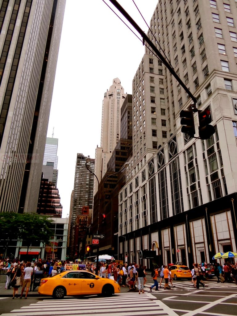 Eine Stadtansicht mit Gebäuden, Ampeln, Fenstern, wenigen Fußgängern, Autos und Himmel.