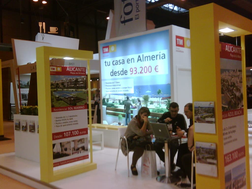 Eine Gruppe von Menschen sitzt an einem Tisch mit einem Laptop, umgeben von verschiedenen Flyern mit Werbung.