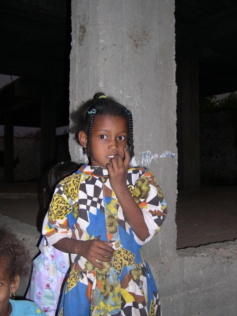 Drei Kinder vor einem Baugerüst stehend, mit dunklem Hintergrund hinter dem Gebäude.