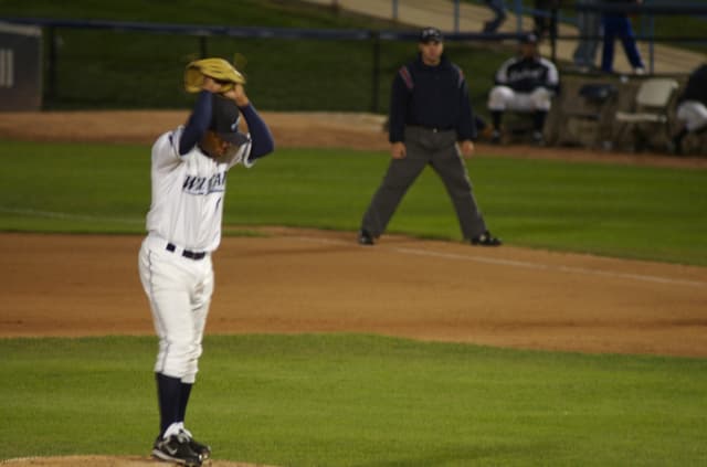 Eine Gruppe von Menschen, die ein Spiel im Freien spielen, mit anderen im Hintergrund auf Stühlen sitzend, umgeben von einem Zaun und Gras.