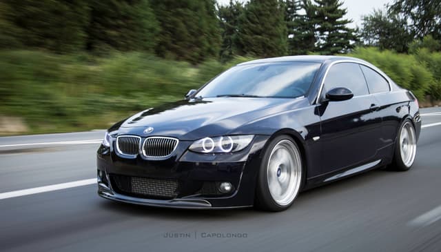 Ein schwarzes BMW Auto fährt auf einer Straße mit Bäumen im Hintergrund.