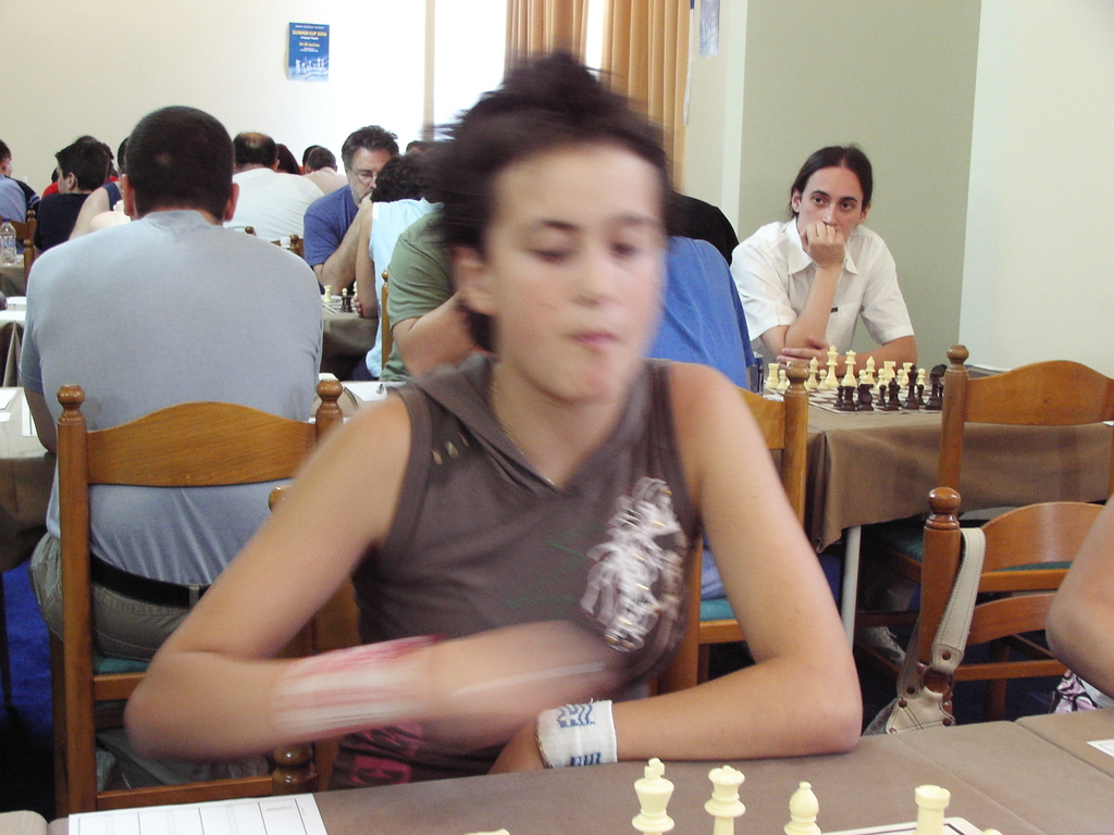 Ein Raum mit Menschen an Tischen beim Schachspielen, eine Vorhangwand und ein Foto in der Ecke.