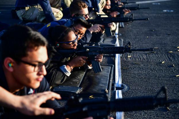 Eine Gruppe von Menschen auf dem Boden sitzend, jeder hält ein Gewehr in der Hand, mit Patronen auf der Straße vor ihnen während eines Trainings.
