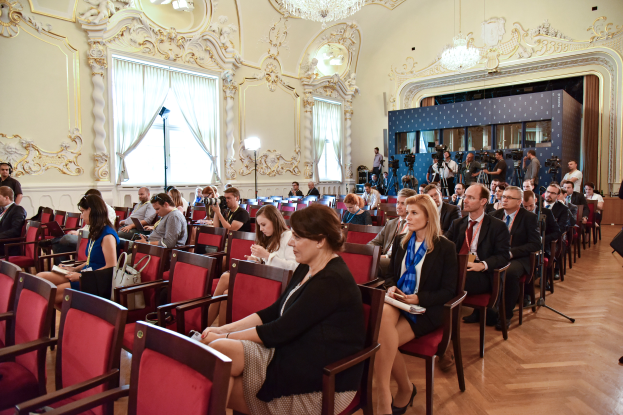 Eine große Gruppe von Menschen sitzt in einem Raum mit einer Wand, Fenstern mit Vorhängen, Stativen und Kronleuchtern an der Decke, einige halten Kameras und besuchen eine Pressekonferenz in Moskau.