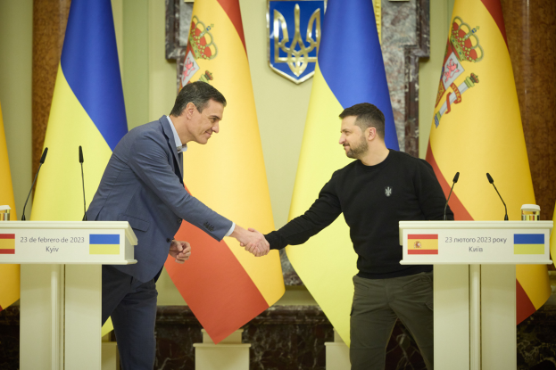 Zwei Männer in formeller Kleidung geben sich die Hand vor Flaggen, mit Mikrofonen auf Podesten und einem Logo im Hintergrund, was ein diplomatisches Ereignis im Zusammenhang mit der Ukraine-Kyrgyzstan-Vereinbarung vermuten lässt.