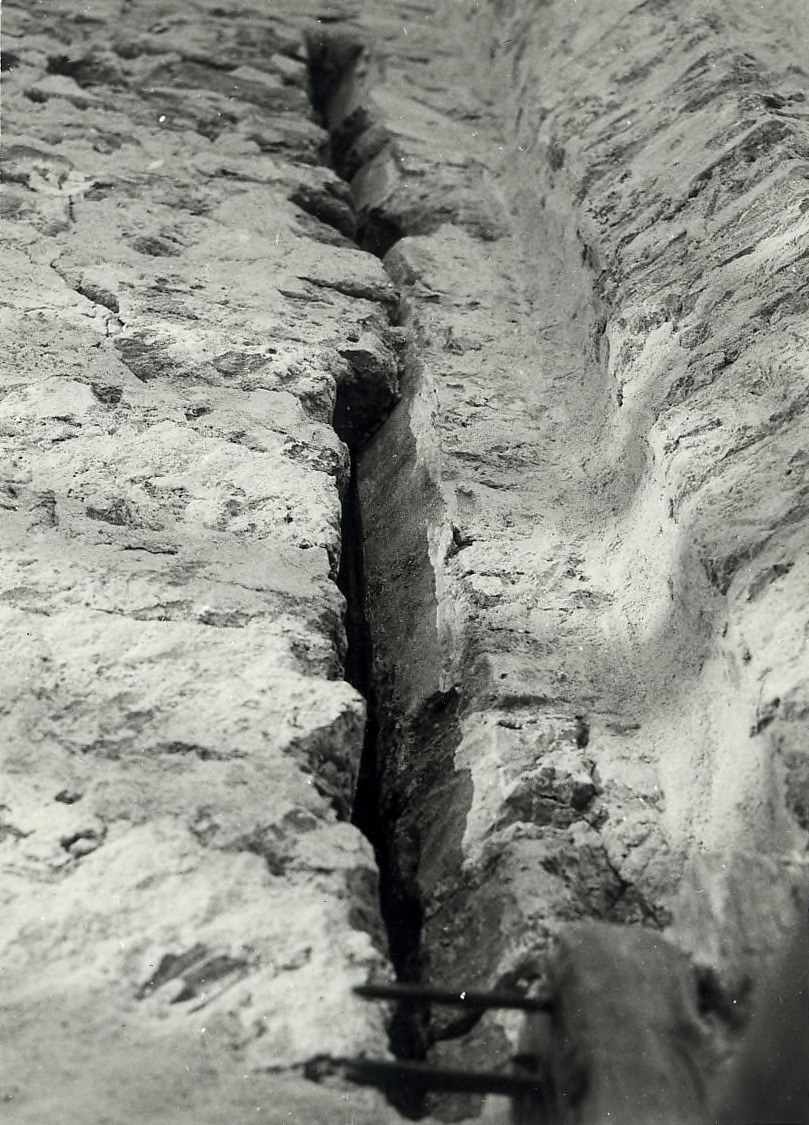 Schwarzes und weißes Foto eines große Riss im Boden, wahrscheinlich ein Entwässerungskanal, mit einem sichtbaren Wasserzeichen auf der linken Seite.