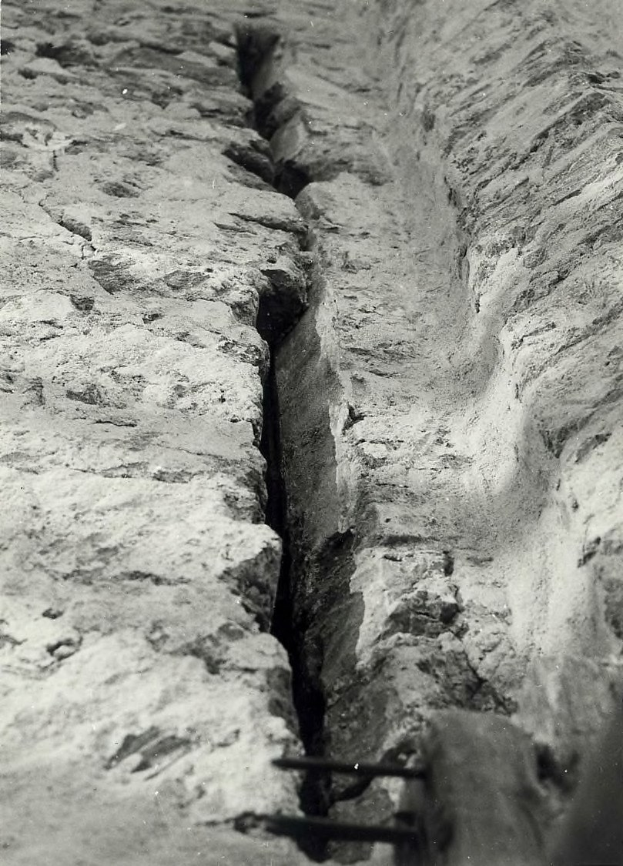 Schwarzes und weißes Foto eines große Riss im Boden, wahrscheinlich ein Entwässerungskanal, mit einem sichtbaren Wasserzeichen auf der linken Seite.