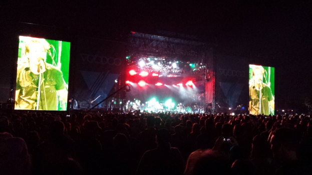 Eine Konzerthalle mit einer Menschenmenge unten, einem großen Bildschirm links und einem kleineren rechts.