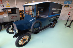 Ein altes Modell-T-Fahrzeug wird in einem Museum ausgestellt, umgeben von anderen Fahrzeugen, mit einem Feuerlöscher und Holzplanken an der rechten Wand.