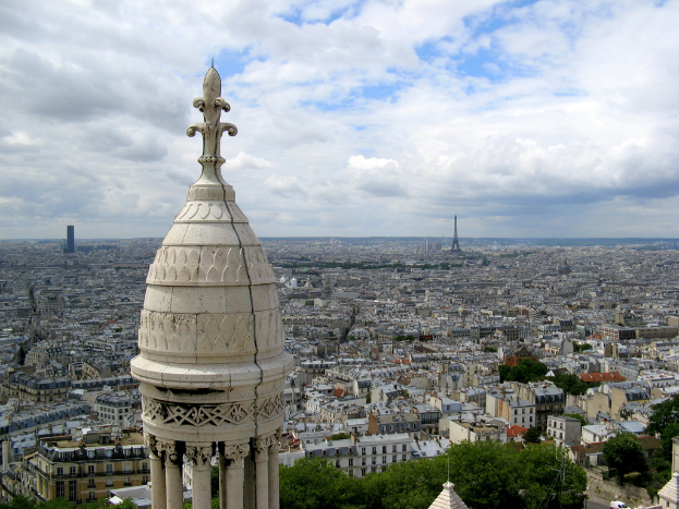 Luftaufnahme einer Stadt mit Türmen, Gebäuden, Bäumen und einem bewölkten Himmel.