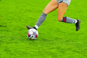 Eine Frau in einem Sportoutfit und -schuhen schießt einen Fußball auf einem saftig grünen Feld.