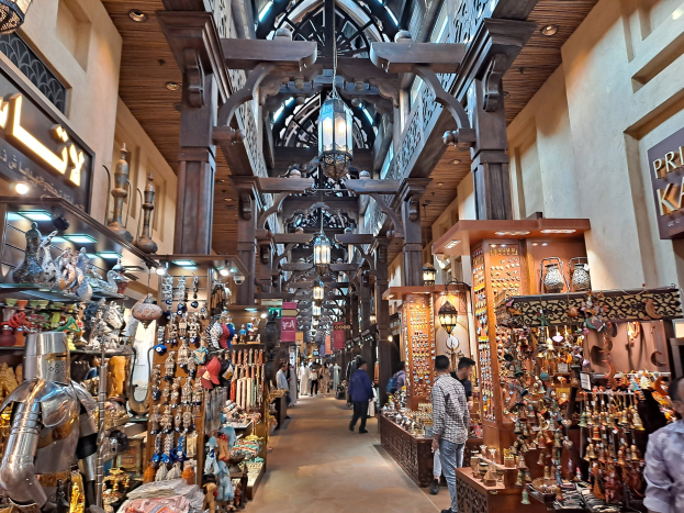 Ein geschäftiges Dubai-Markt mit Menschen, die zwischen Regalen voller Waren hindurchgehen, Texttafeln an den Wänden und einer Decke mit warmem Licht.