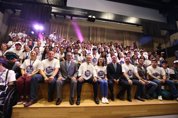 Eine Gruppe von Menschen auf einer Bühne mit einer Person im Rollstuhl links, vor einem Vorhang, Scheinwerfern und einer Wand auf einer NBA-Frauenbasketballkonferenz.