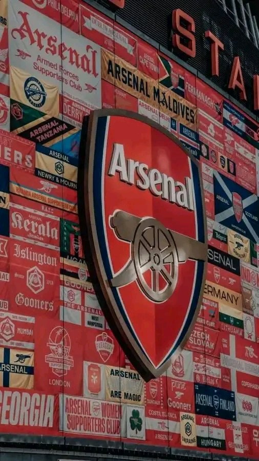 Arsenal FC-Logo auf der Seite eines Gebäudes mit Begleitbannern und Fahnen sowie Texttafeln unten.