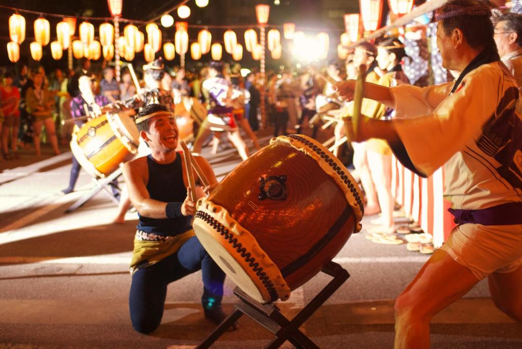 Männer spielen Trommel bei einem Festival mit Lichtern darüber.