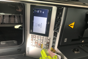 Eine Nahaufnahme eines Geräts mit Touchscreen, Knöpfen und einer Glasfenster, das das Innere eines Fahrzeugs zeigt.