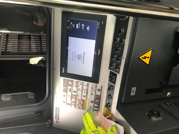 Eine Nahaufnahme eines Geräts mit Touchscreen, Knöpfen und einer Glasfenster, das das Innere eines Fahrzeugs zeigt.