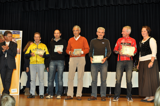 Eine Gruppe von Menschen steht auf einer Bühne und hält Zertifikate in den Händen, mit einem Banner und einem Tisch dahinter und einem schwarzen Vorhang neben dem Tisch.