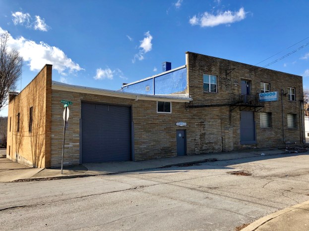 Ein altes Backsteingebäude an einer Straßenecke mit Fenstern, Türen, einem Schild an einem Pfahl, Bäumen, Kabeln und einem bewölkten Himmel, zum Verkauf angeboten für 1.250.000 USD.