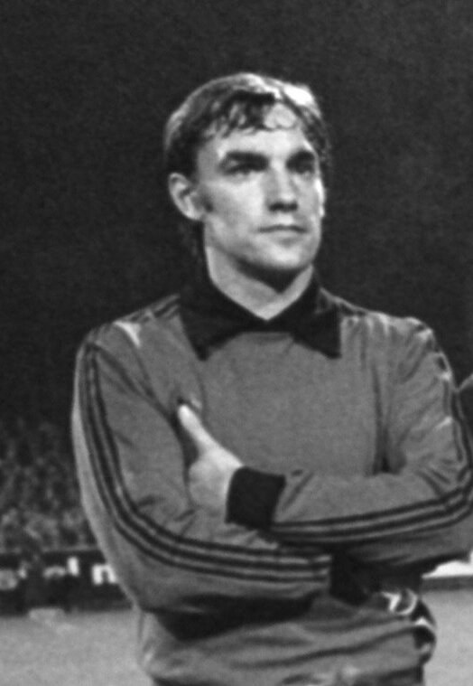 Schwarzes und weißes Foto eines Mannes auf einem Fußballfeld mit verschränkten Armen, umgeben von sitzenden Zuschauern, der angeblich der legendäre Torwart von Manchester United ist, der im Alter von 89 Jahren starb.