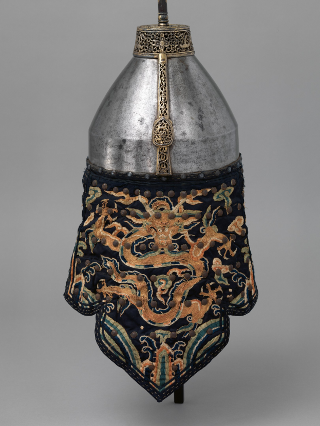 Metallhelm mit einer Drachengestaltung, vor einem grauen Hintergrund, mit detaillierter Metallarbeit.