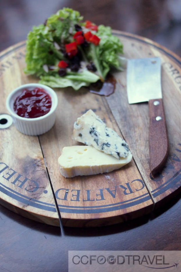 Ein hölzernes Schneidbrett mit Blattgemüse, einem Becher, einem Messer und etwas Essen, mit Text unten.