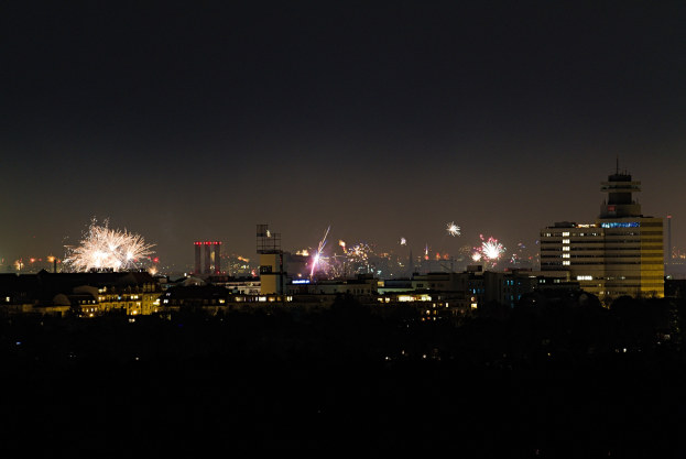 Eine nächtliche Stadtpanoramaaufnahme mit beleuchteten Gebäuden und Feuerwerk am Himmel.