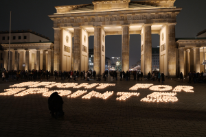 Eine Gruppe von Menschen vor dem beleuchteten Reichstagsgebäude in Berlin, Deutschland, mit den Worten 'Kämpfe für die Freiheit' im Vordergrund geschrieben.