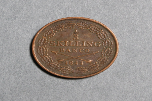 Copper coin with the text "Skilling Banco" resting on a gray surface.