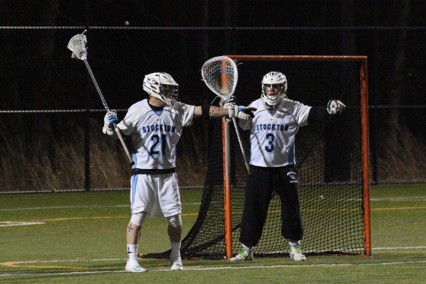Zwei Personen in Sportkleidung stehen auf einem Platz, halten ein Objekt und haben eine Glaswand und ein Tor im Hintergrund.