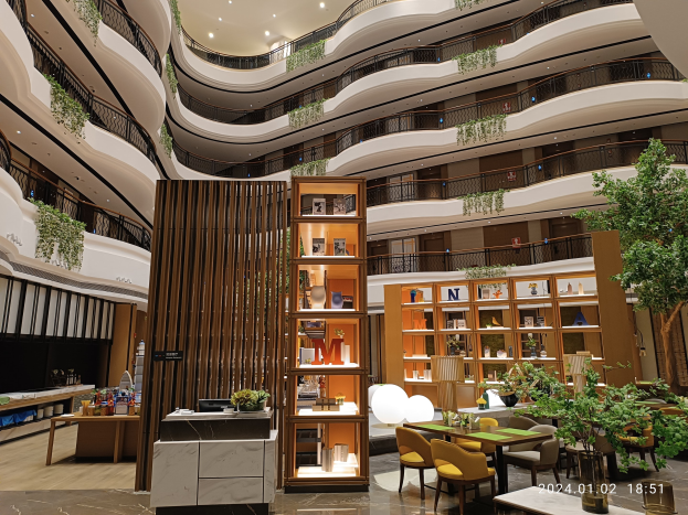 Großer Atrium mit Tischen, Stühlen, Topfpflanzen, Geländern und Beleuchtung in einem Dubai-Hotel-Innenraum.