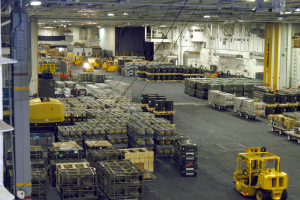 Lagerhalle mit Trucks, Containern, Menschen, Beleuchtung, Metallstangen und sichtbarem Rad.