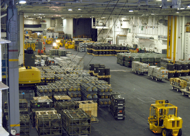 Lagerhalle mit Trucks, Containern, Menschen, Beleuchtung, Metallstangen und sichtbarem Rad.